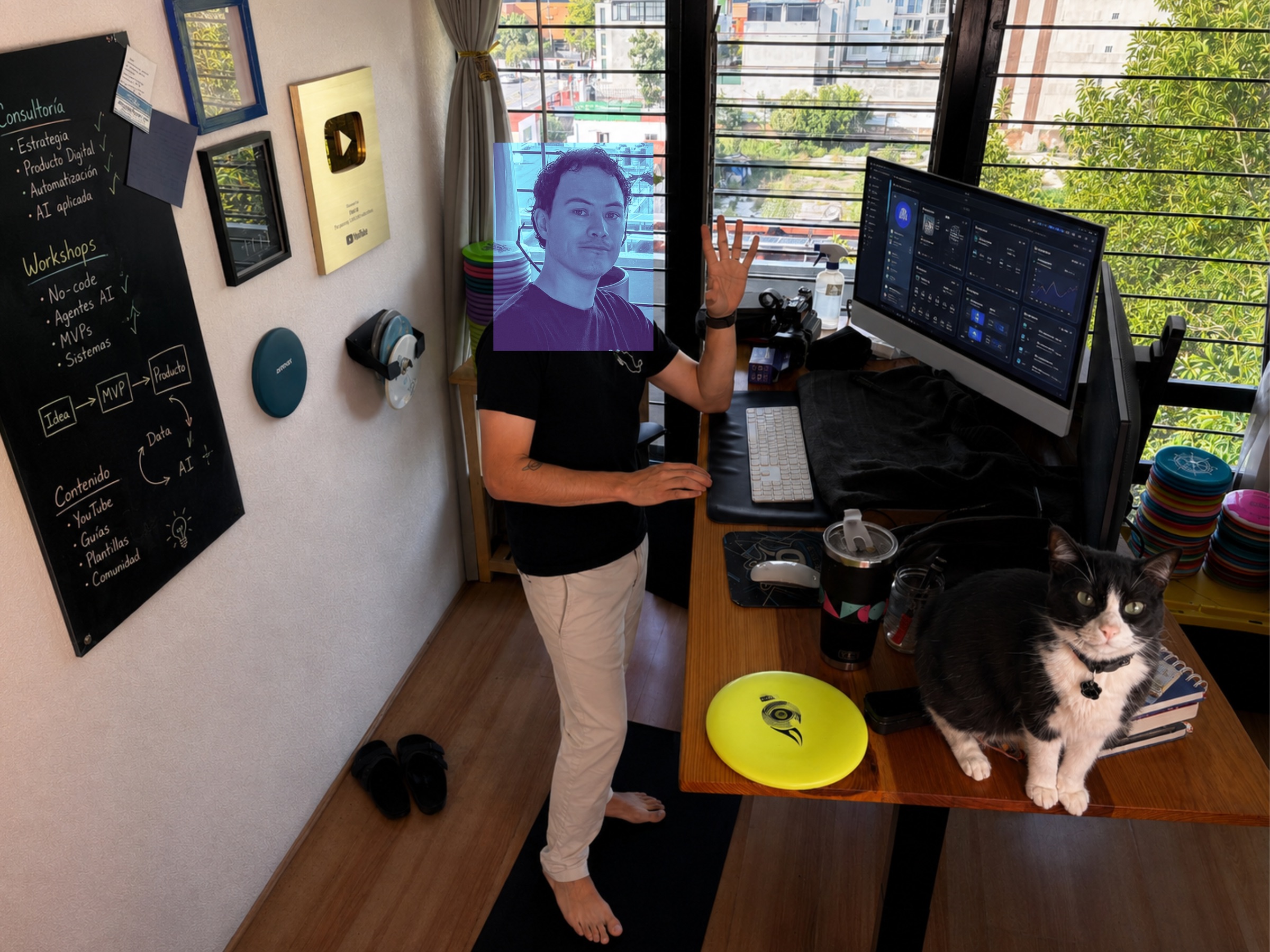 Fabián Oloarte in his workspace with a teaching board, YouTube plaque, product monitor, disc golf equipment, and his cat Rubén.